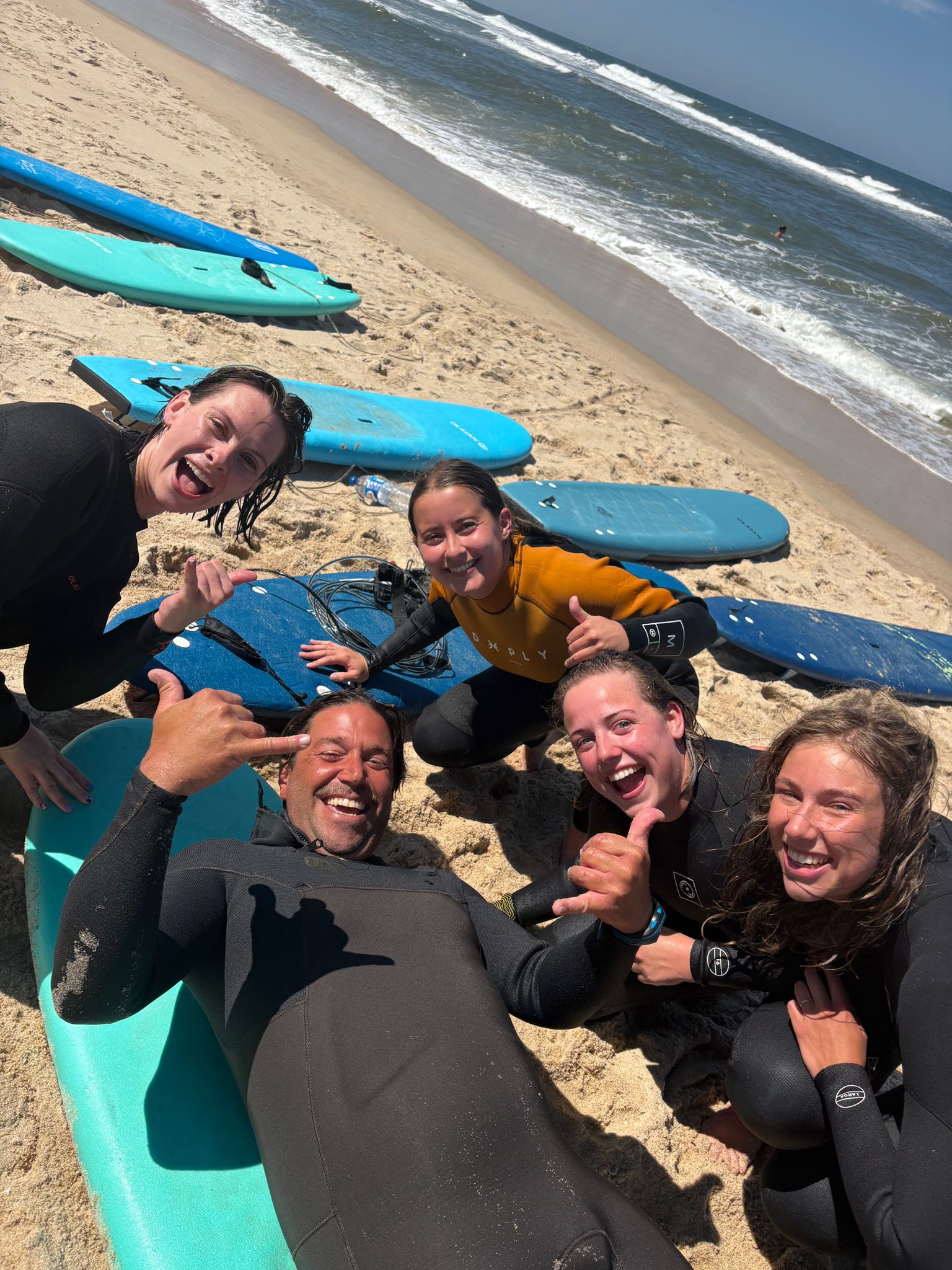 Friends on the beach in wetsuits around a board — surf Gaia, surf Portugal group lesson