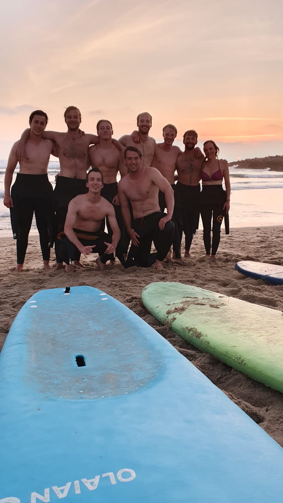 Large group at sunset on the sand with surfboards — surf camp Portugal and Porto coast