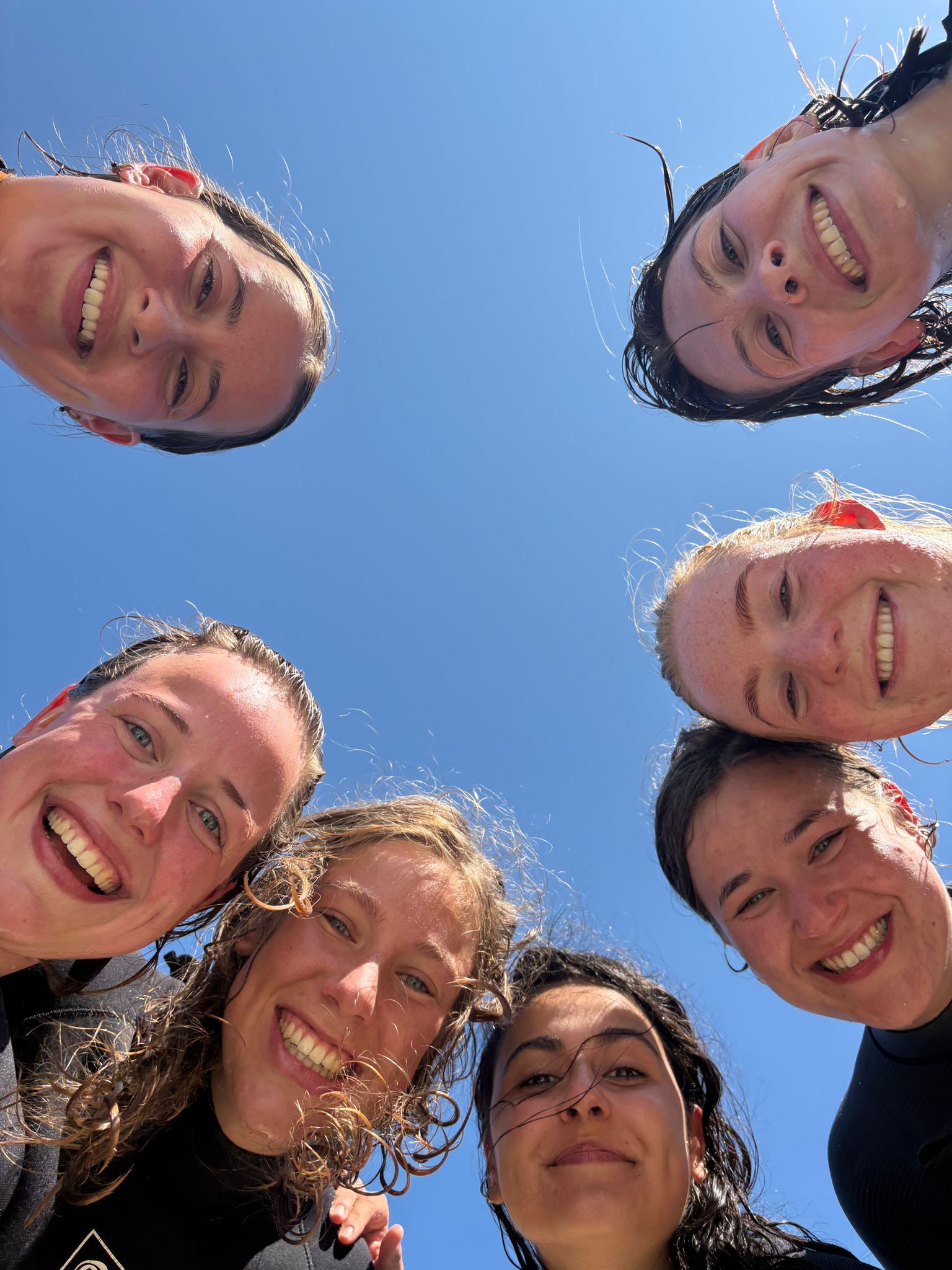 Circle of women in wetsuits under blue sky — surf lessons Porto and Portugal